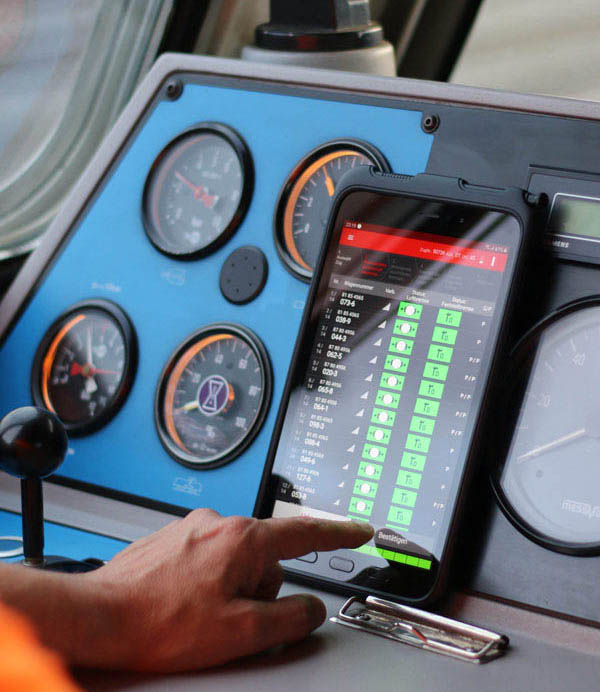 Tablet displaying real-time freight train monitoring data inside a railway vehicle cab, integrated with onboard instrumentation. 