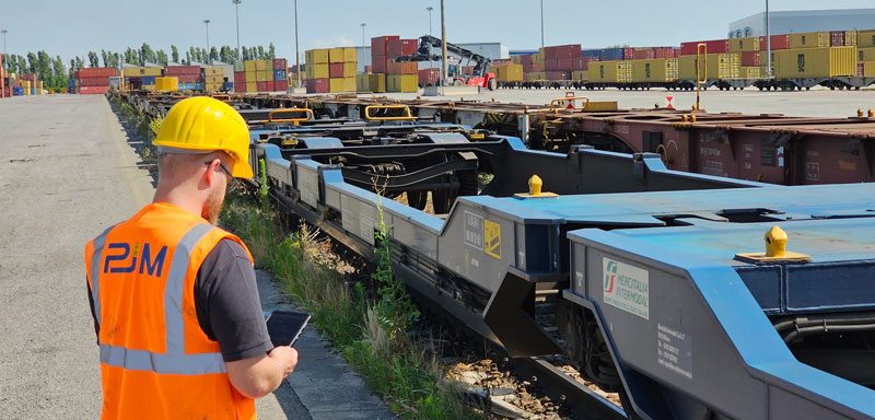 Rail freight wagon equipped for digital brake monitoring, with a railway technician inspecting a freight train at an intermodal terminal.