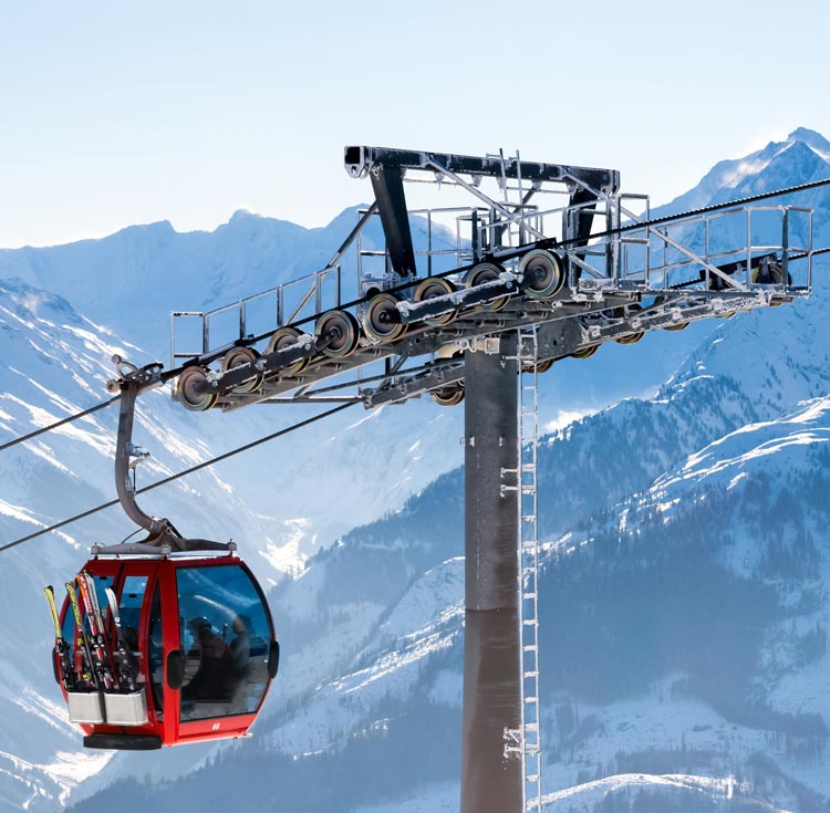 The image shows a red cable car gondola traveling along a steel cable over a snowy mountain landscape.